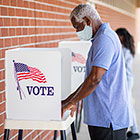 mask-wearing man at outdoor voting booth