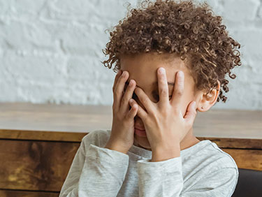 Child holds hands over his face