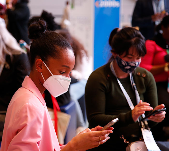 Two women with masks on look down at their phones during the APHA 2022 Tweetup.