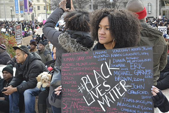 A young Black woman holds a sign during a protest that says #Black Lives Matter. 