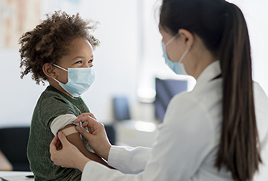 Boy wearing mask receives a vaccination from nurse