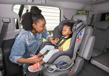 A woman straps a child into a car seat in a car