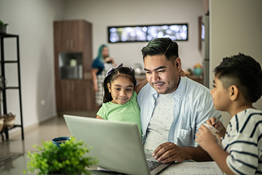 A father and two children work on a computer laptop