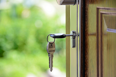 A key on a key ring with two other keys is in a lock to a front door of a house. 