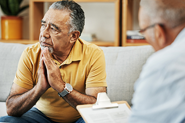 A man sits on a sofa listening to his doctor.