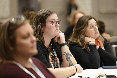 Three people sit at a table and look toward the presentation speaker off camera. 