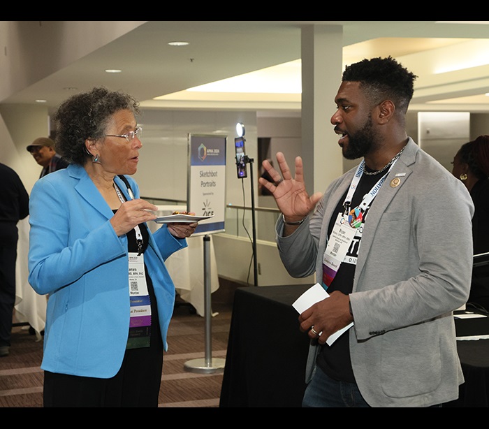 A woman holds a plate while listening to a man talk to her at the APHA President's Reception. 
