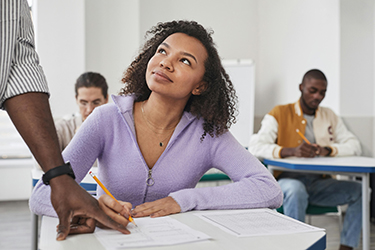 Student sits at desk look up at teacher, whose hand is on desk