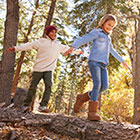 Two children balancing while walking along a fallen log in a forest. 