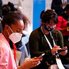 Two women with masks on look down at their phones during the APHA 2022 Tweetup.