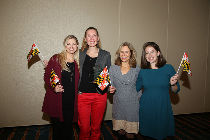 four smiling women waving state of Maryland flags